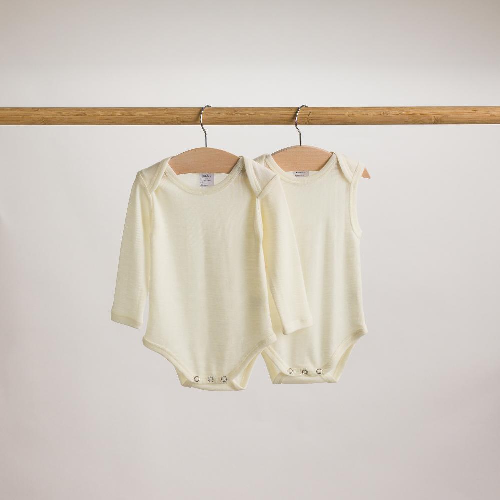 Two baby merino cream baby bodysuits hanging on a wooden rod against a plain background