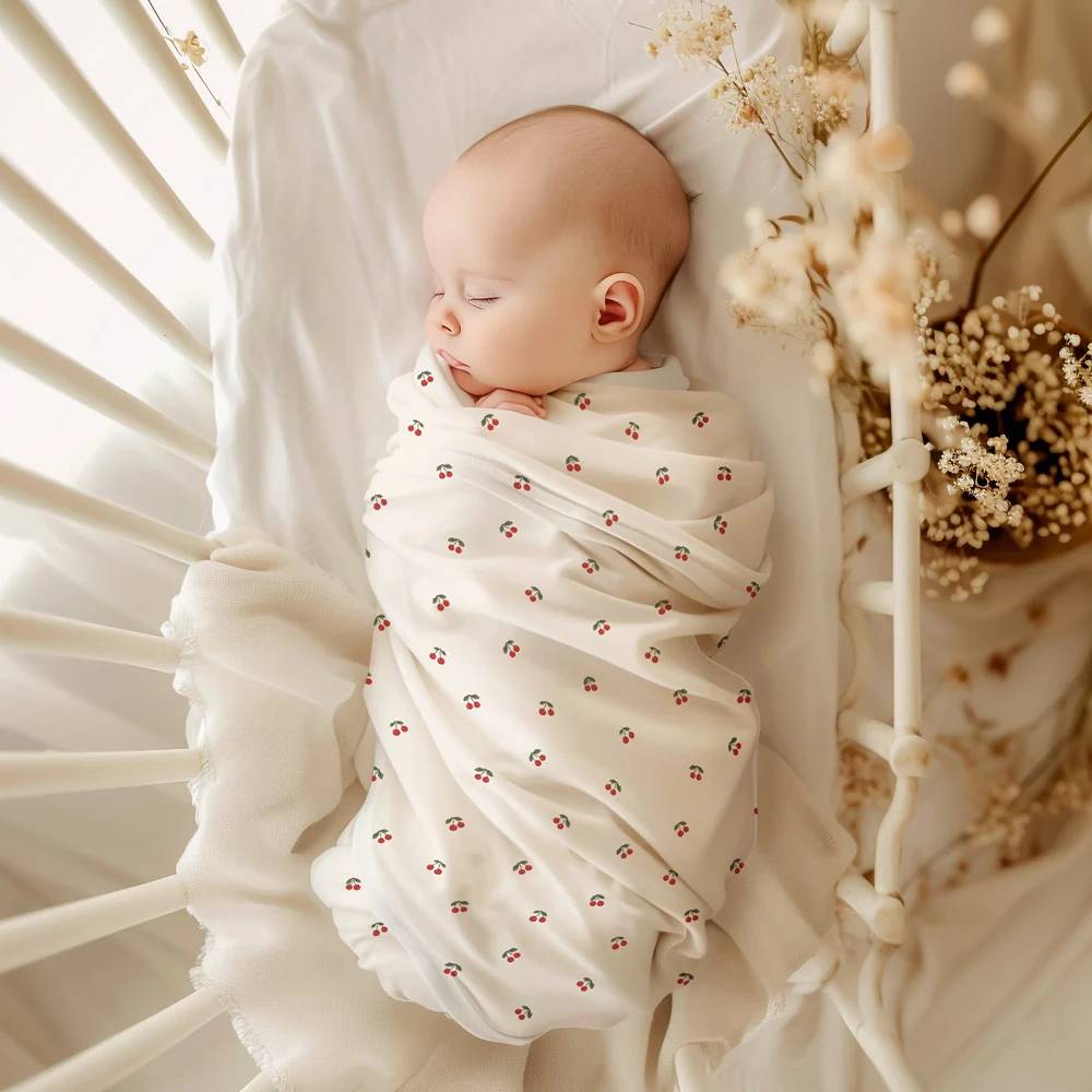 A sleeping baby in a cot wrapped in a stretchy swaddle with a cherry pattern.