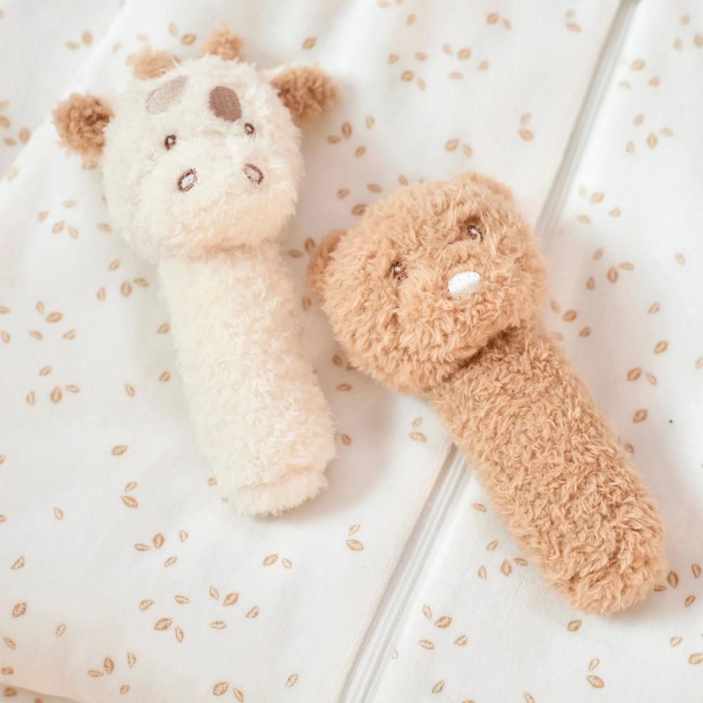 Two plush rattle toys, one white and one brown, on a textured surface.