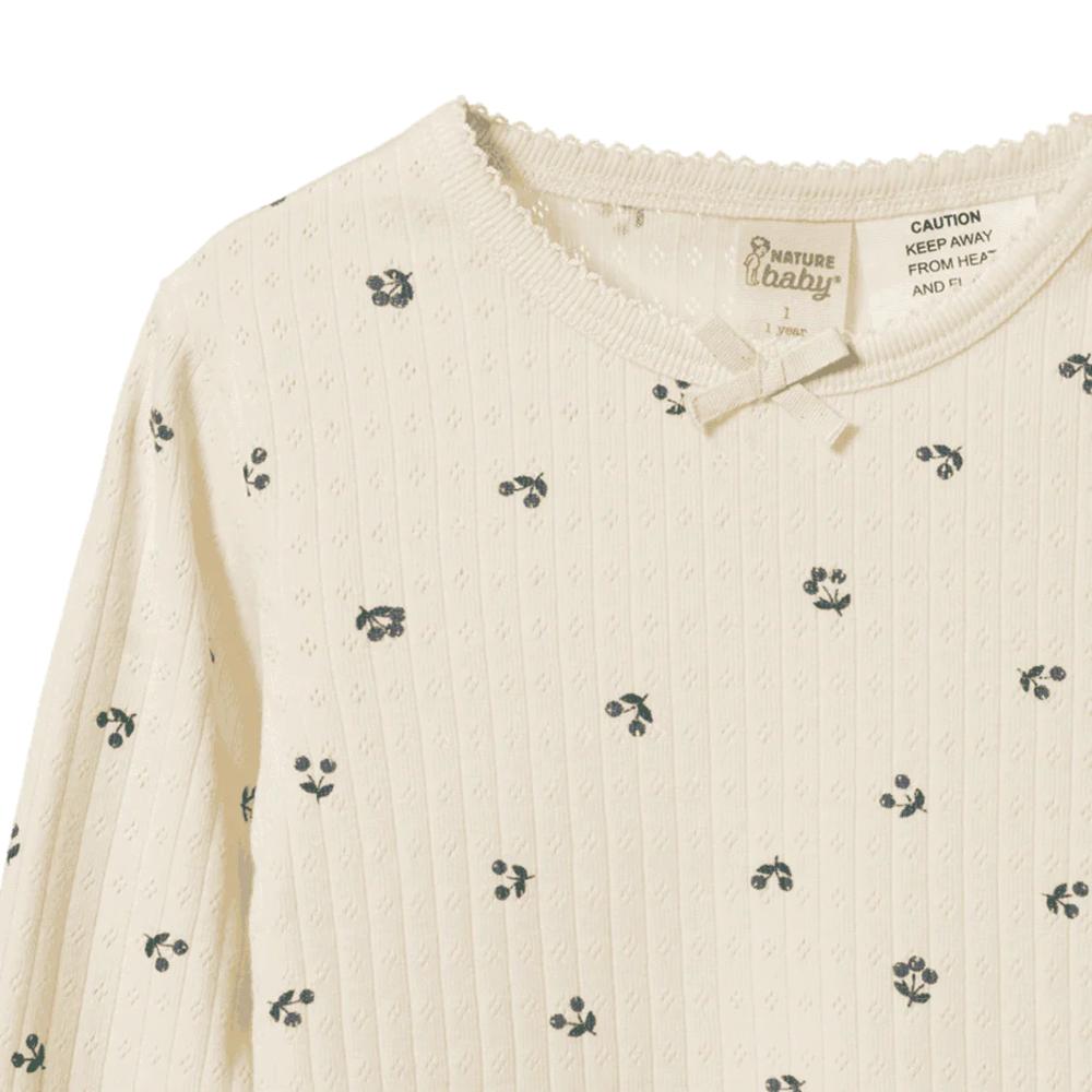 Cream baby pyjama top with dark purple berry pattern and 'Nature Baby' label on a white background