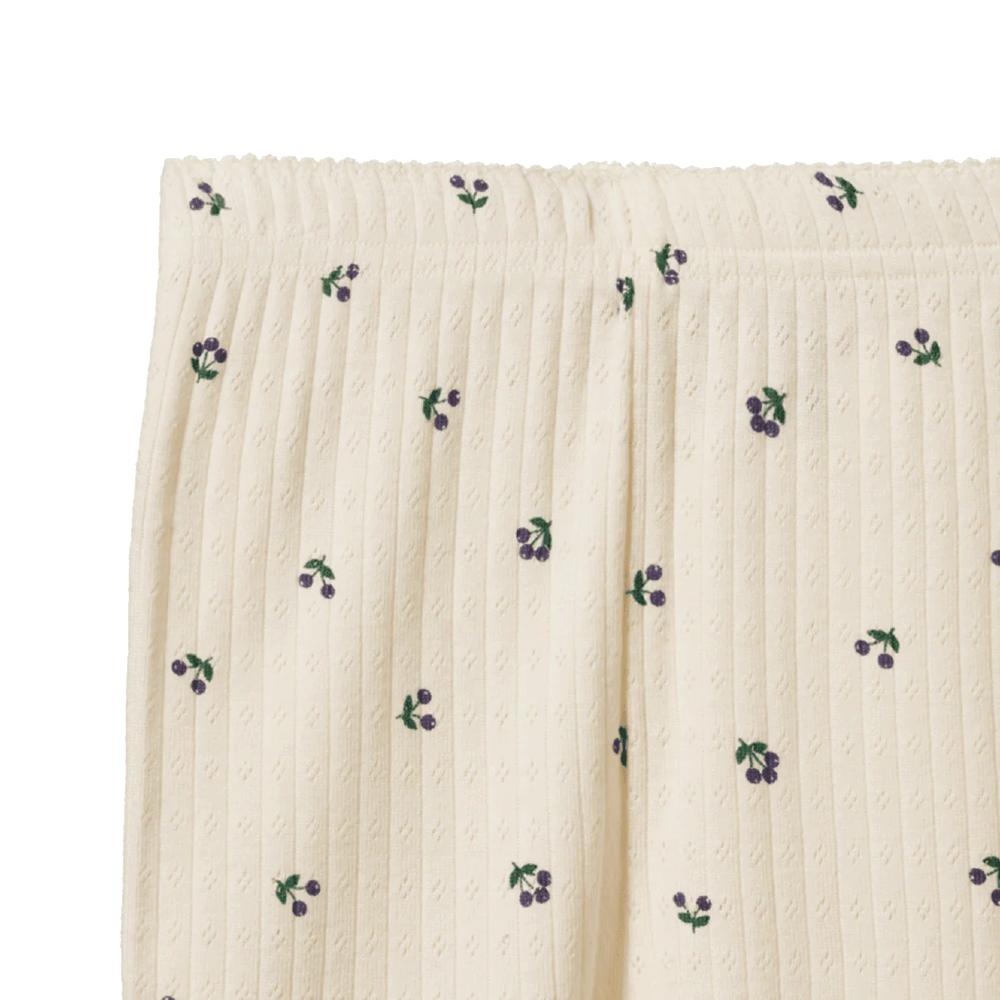 Textured cream pointelle fabric with small green and purple berry patterns on a white background