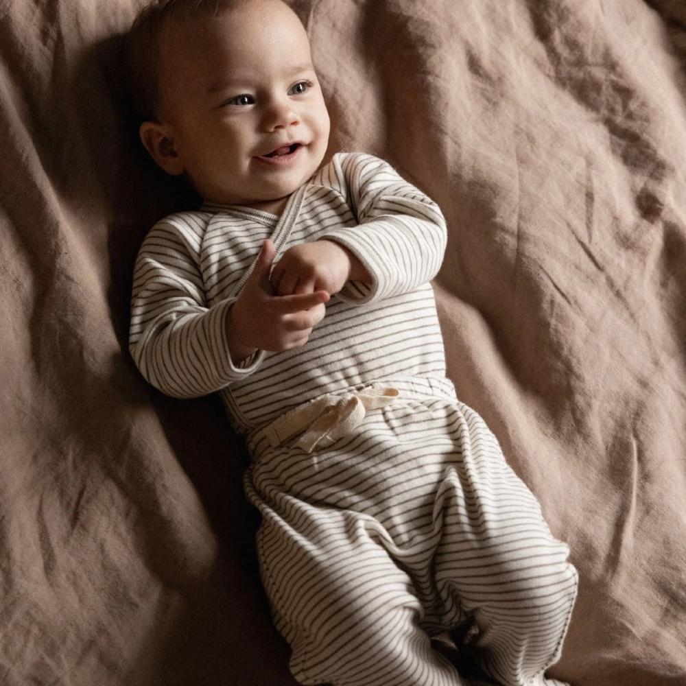 Baby in a matching cream and brown striped outfit lying on a soft brown surface