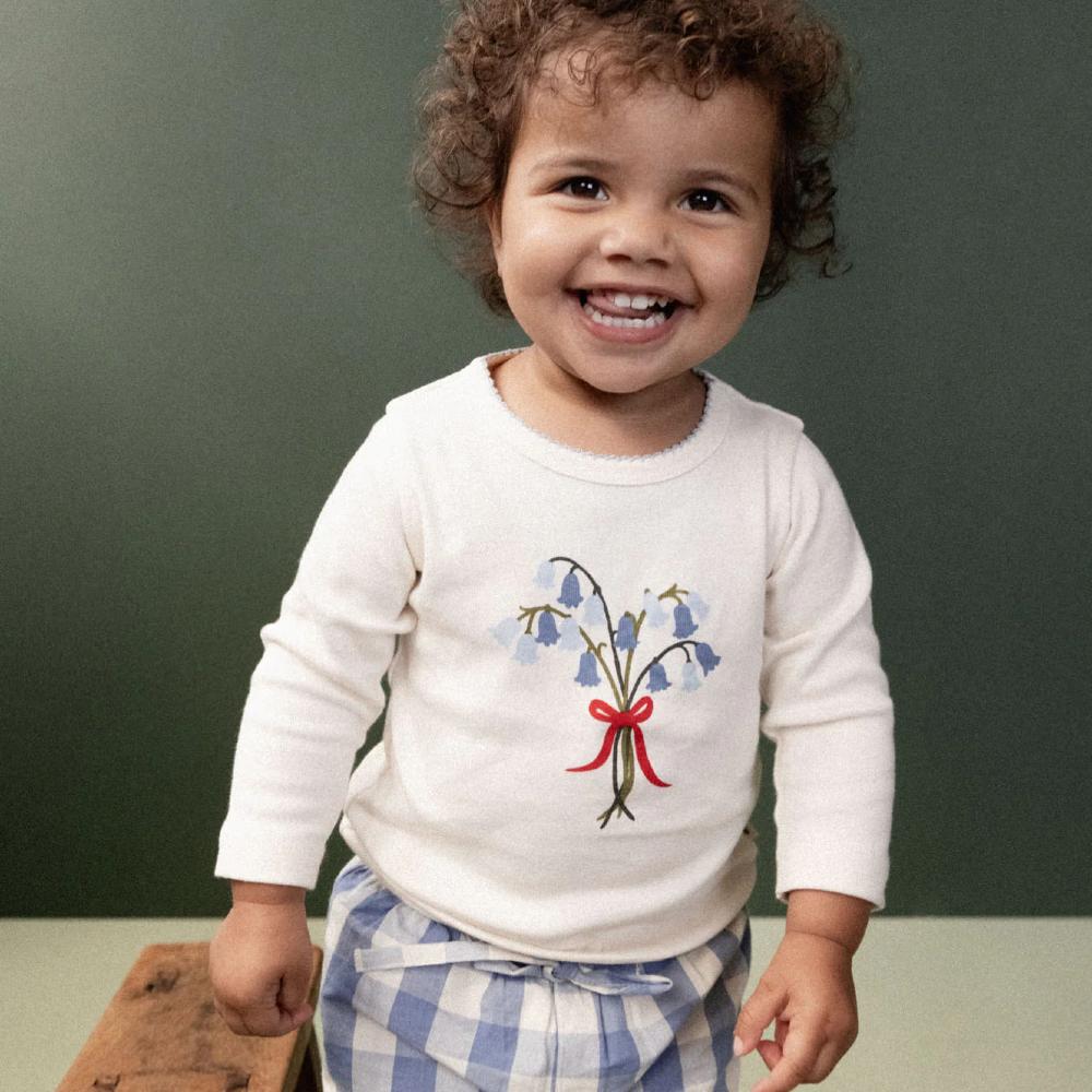 Child wearing a white cotton long sleeve shirt with a bluebell floral design against a green background