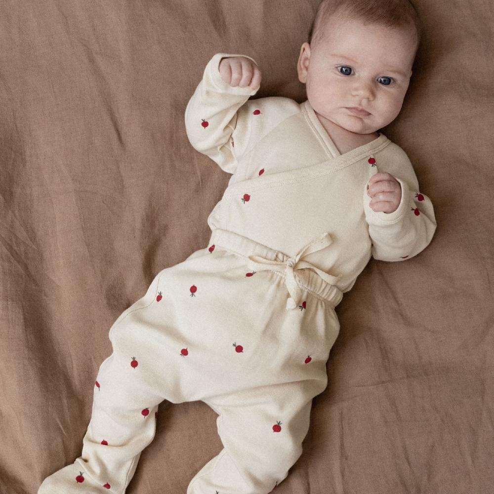 Baby wearing a cream outfit with red radish patterns lying on a brown surface