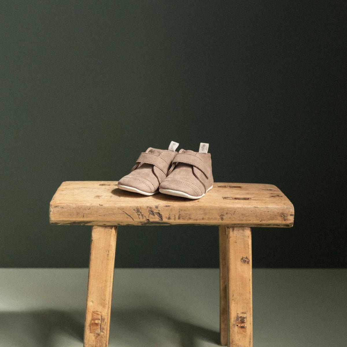 Pair of brown baby shoes on a wooden stool against a dark green background