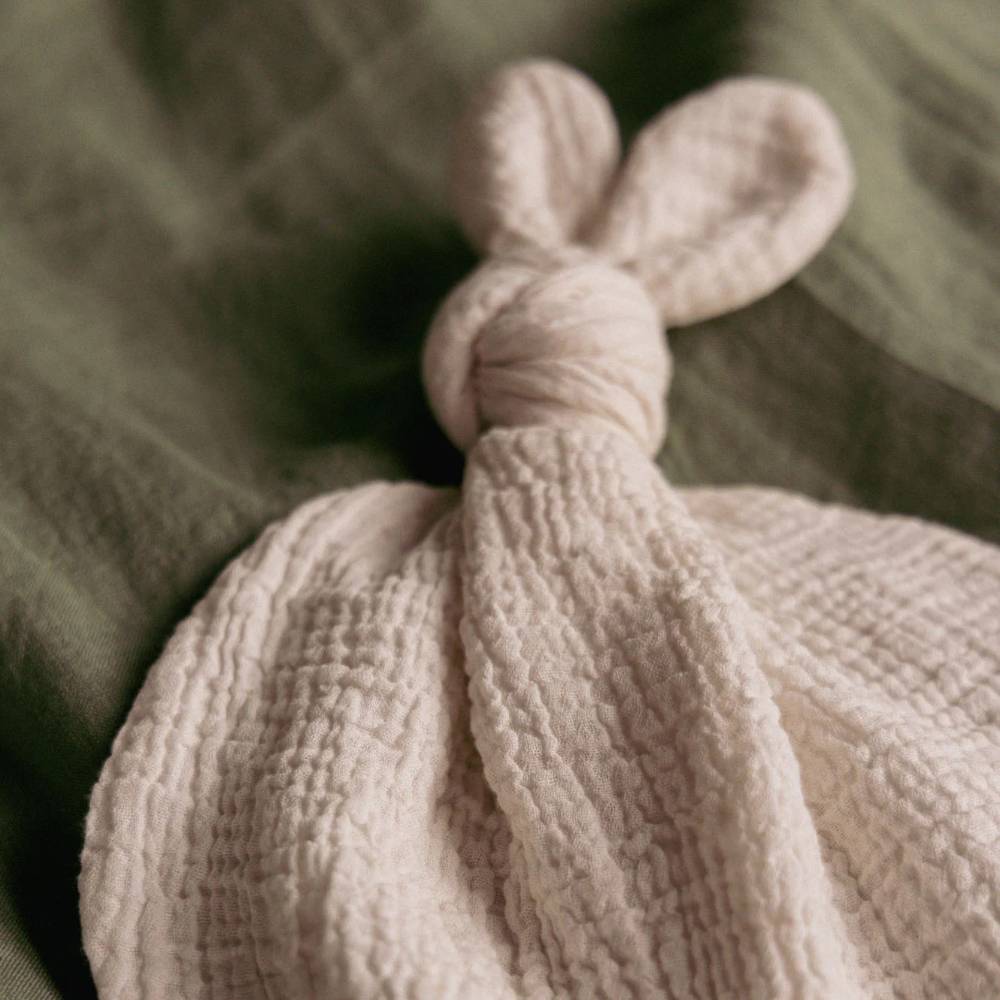 Textured beige knot toy with bunny ears on a soft green background