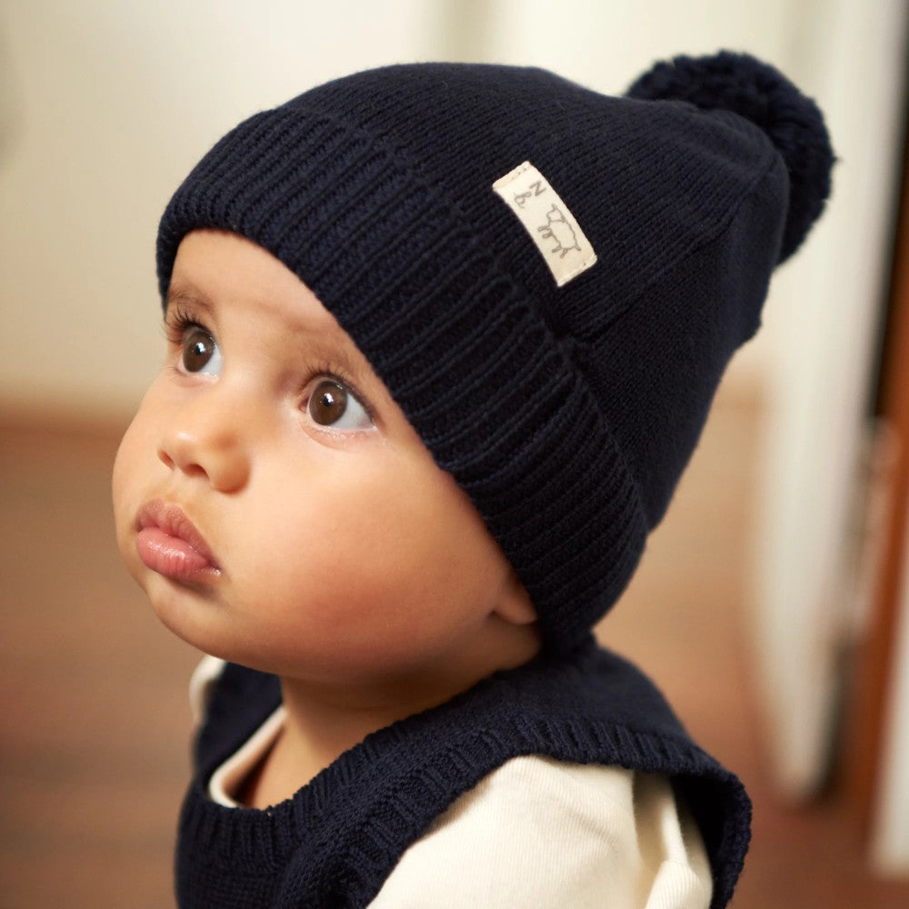 Child wearing a navy blue knit hat with a pom-pom on a blurred background