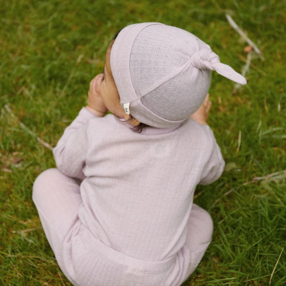 Baby in a light purple merino pointelle outfit and hat sitting on grass