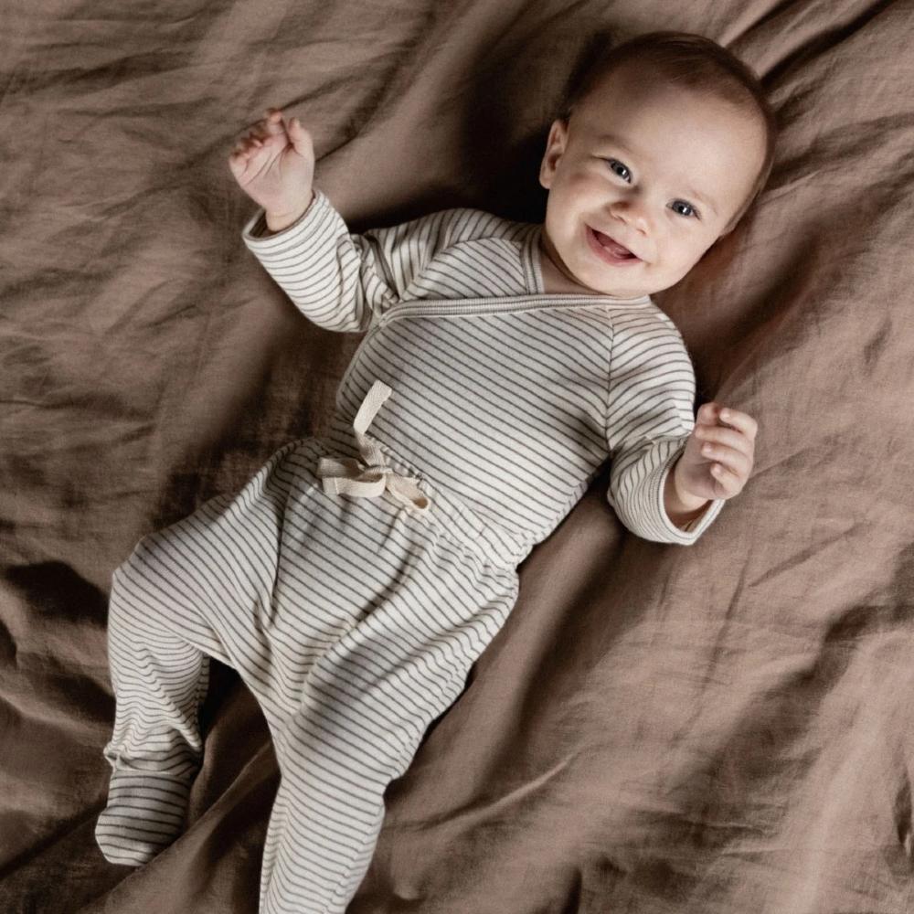 Baby in a brown and cream striped kimono bodysuit and matching footed leggings lying on a brown linen duvet cover