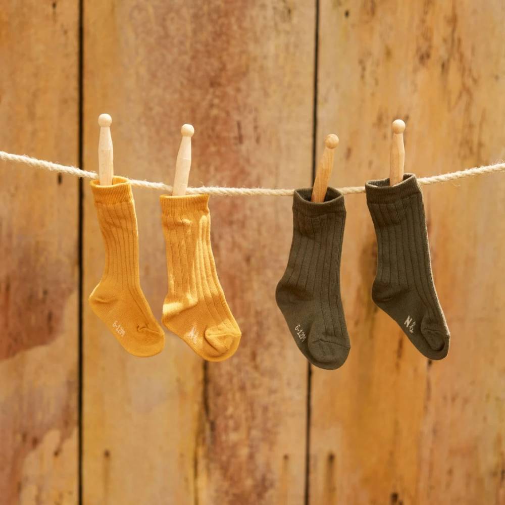 One pair of yellow and one pair of dark green cotton rib socks hanging on a clothesline against a wooden background