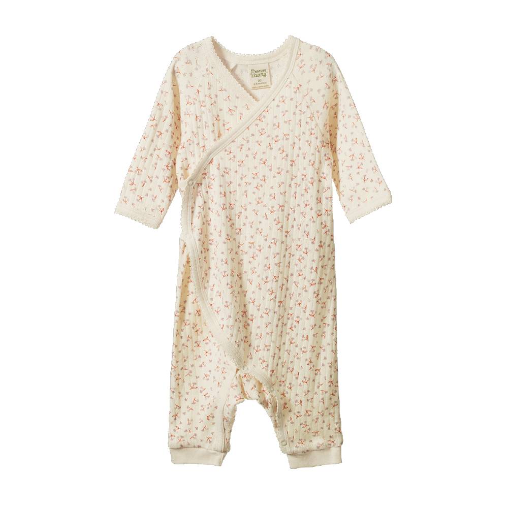 A baby long-sleeve footless onesie in cream cotton muslin with a tiny pink and green floral print, featuring a wrap-style front and snap closures.