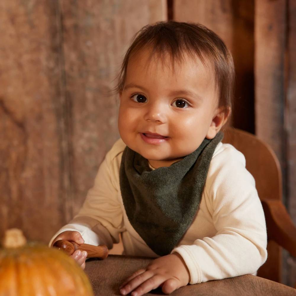 Child wearing a bib sitting at a table with a pumpkin, smiling.