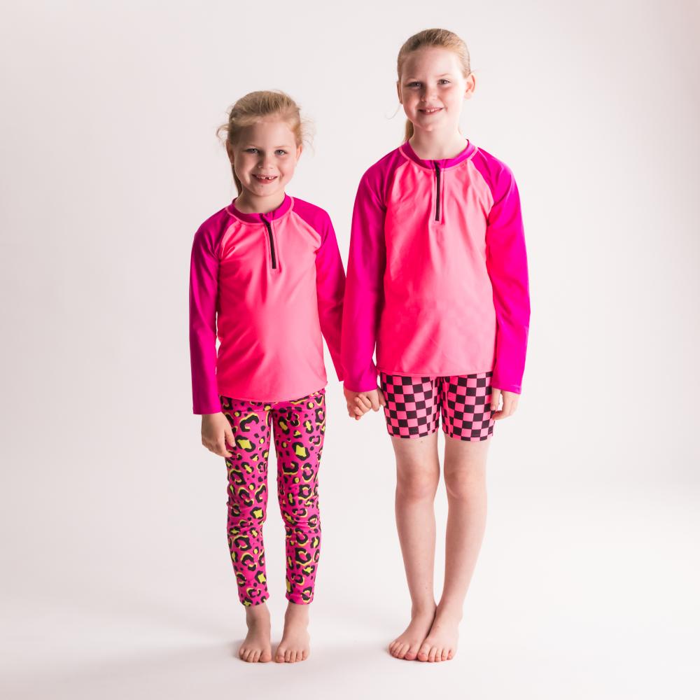 Two children wearing matching pink outfits with leopard print pants on a white background
