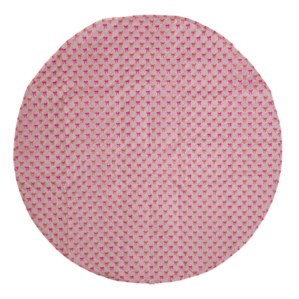 A circular play mat, or coaster, featuring a repeating pattern of small pink bows on a light pink background.