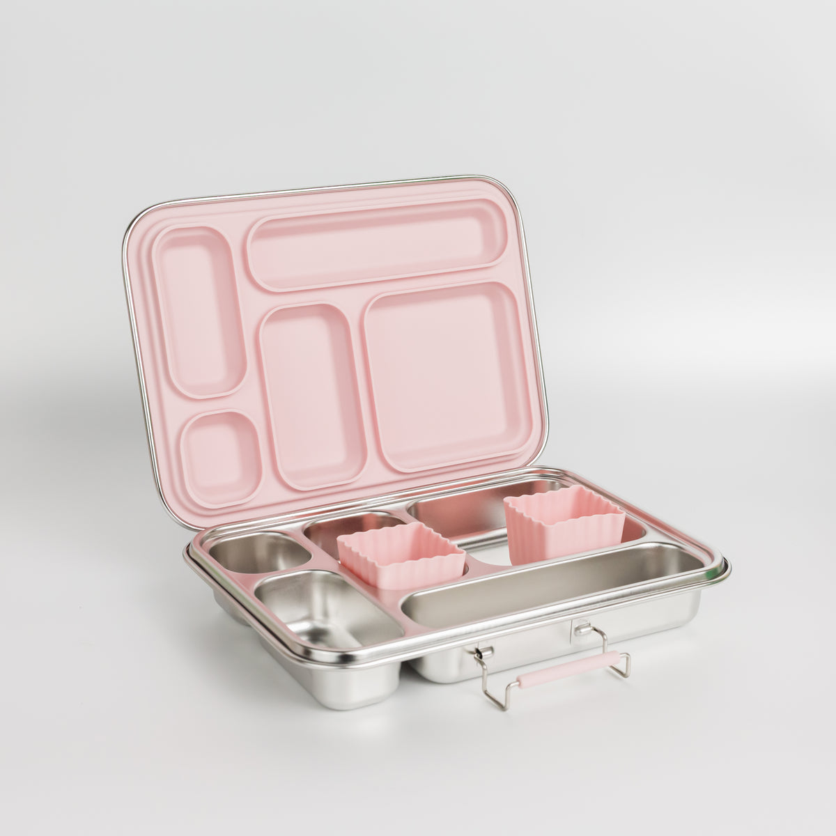 An open stainless steel bento lunch box with a pink interior and compartments, including two small pink silicone insert pieces, shown on a light gray studio background.
