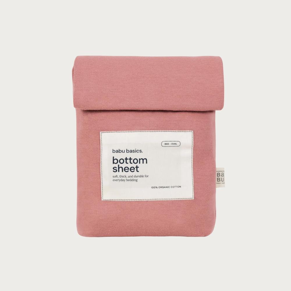 A dusty pink cotton bottom sheet by babu basics, folded and presented flat against a light gray background with a white product label on the front.