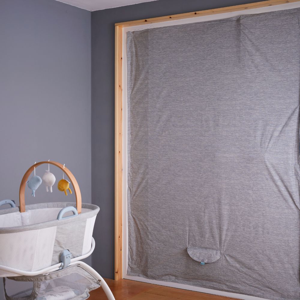 Nursery room with a crib and baby mobile against a gray wall with portable blackout blind