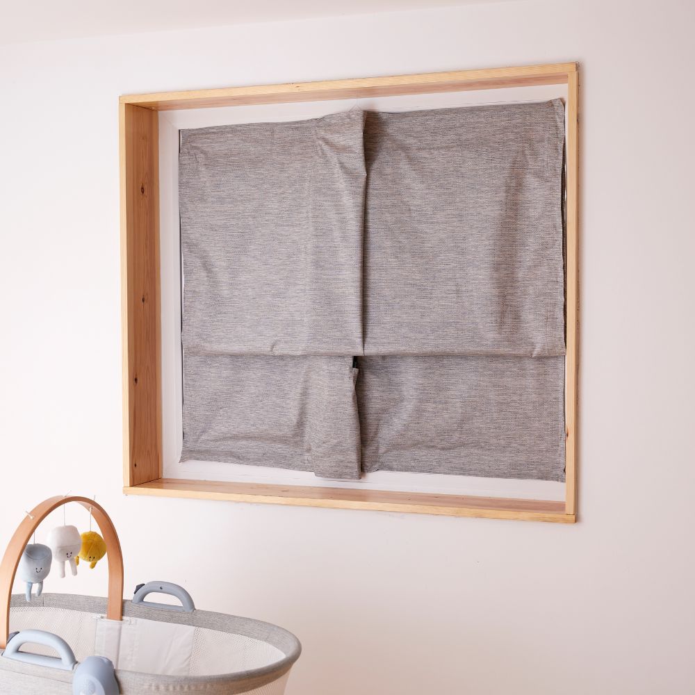 Gray blakcout blind displayed in a wooden frame against a light wall.