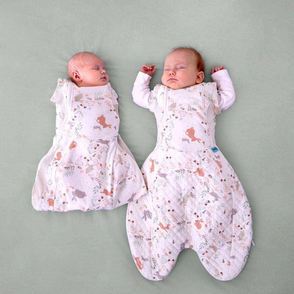 Two newborn babies wearing patterned sleep sacks with arms in and out on a plain background