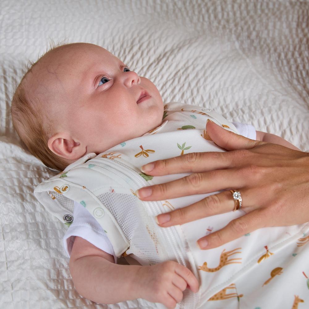 Baby wrapped in a swaddle with animal patterns, lying on a textured surface.