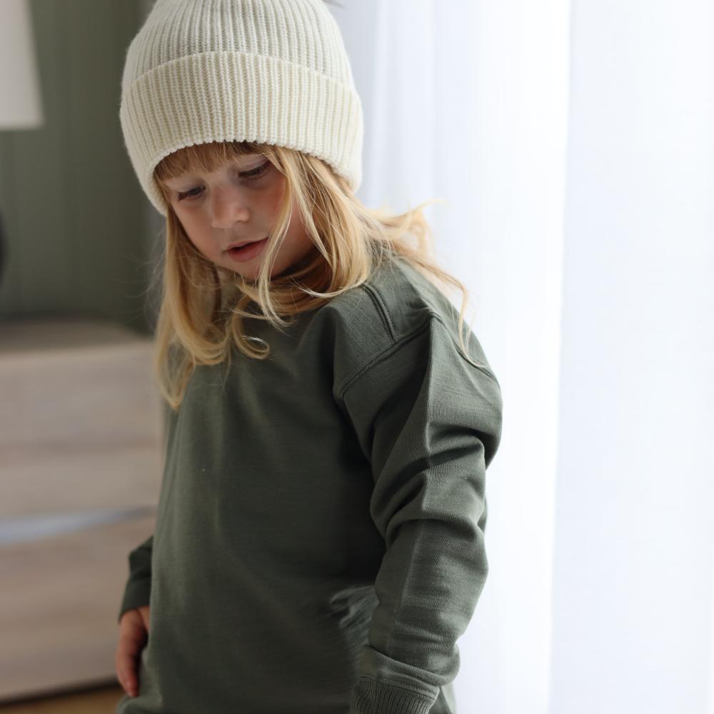 Child wearing a green sweater and Cream merino knit hat indoors