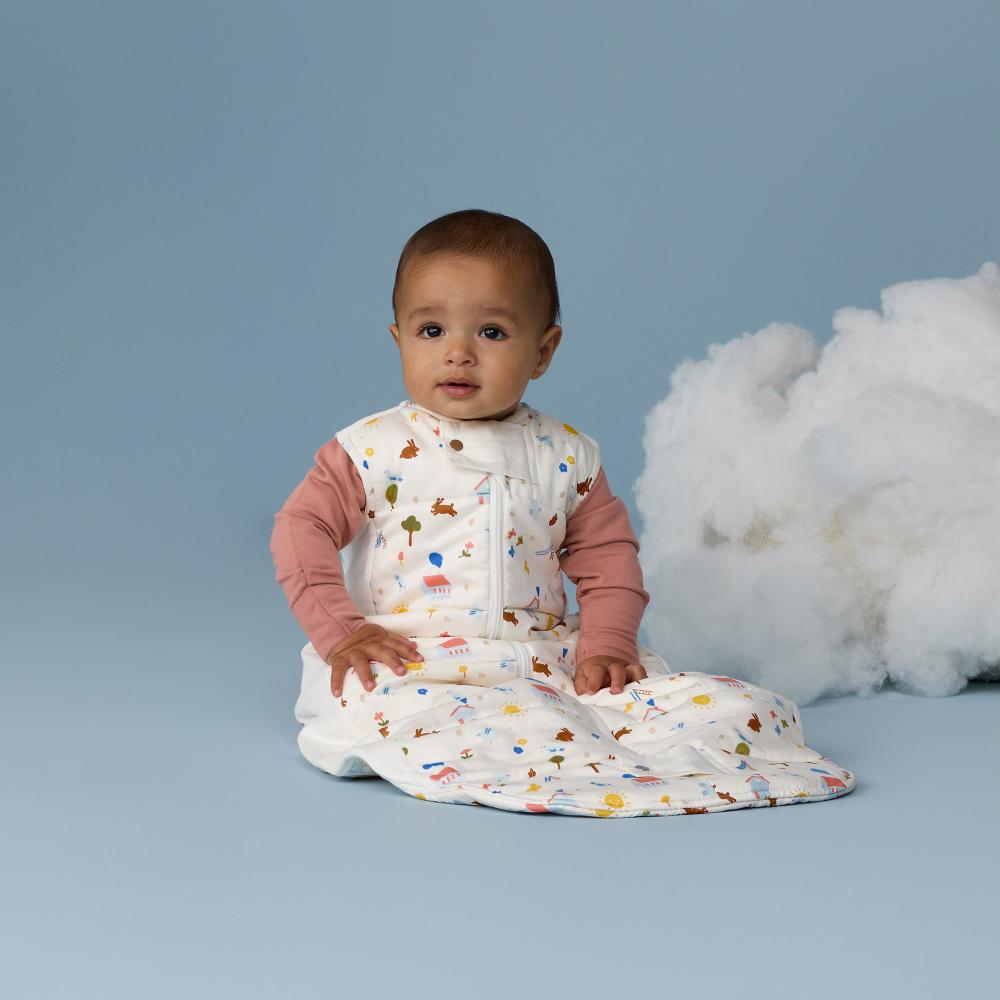 Baby sitting on a blue surface with a white fluffy cloud-like object, wearing a colorful outfit.