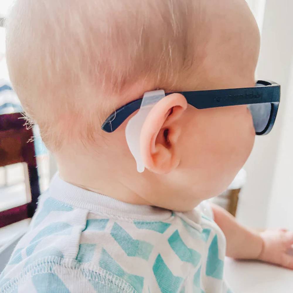 Close-up of a baby wearing dark navy blue baby sunglasses with a clear silicone ear hook and gray lenses.