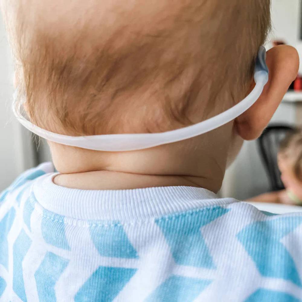 Baby wearing a blue and white patterned bib with a clear strap over the head.
