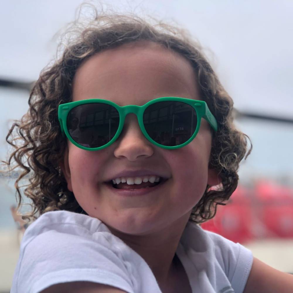 Child wearing round green ro.sham.bo  sunglasses with a blurred background