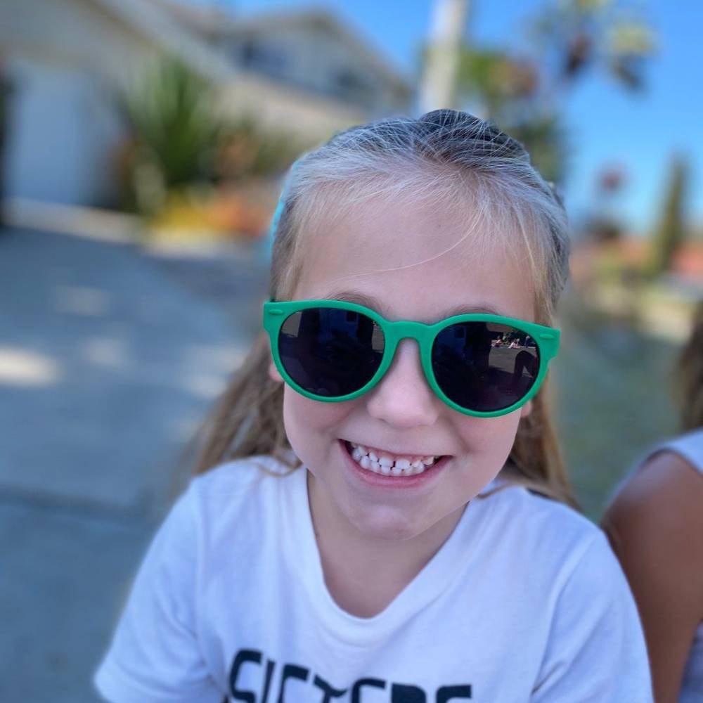 Child wearing green round ro.sham.bo sunglasses with a blurred outdoor background