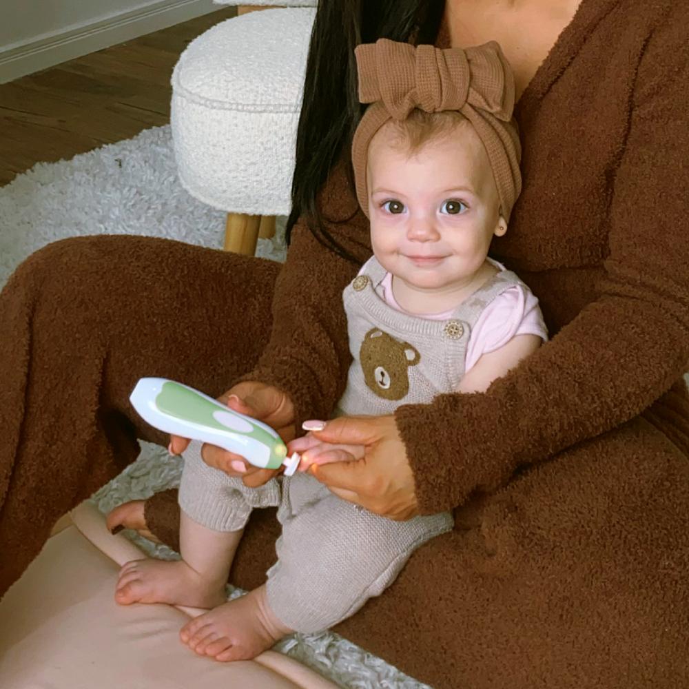 Baby with bow smiling while having nails shortened with electric nail care set in a home setting 