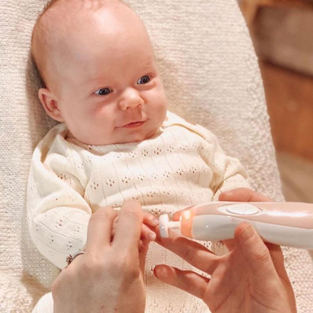 Baby in a cream outfit with an electric nail care set being used on their small hand