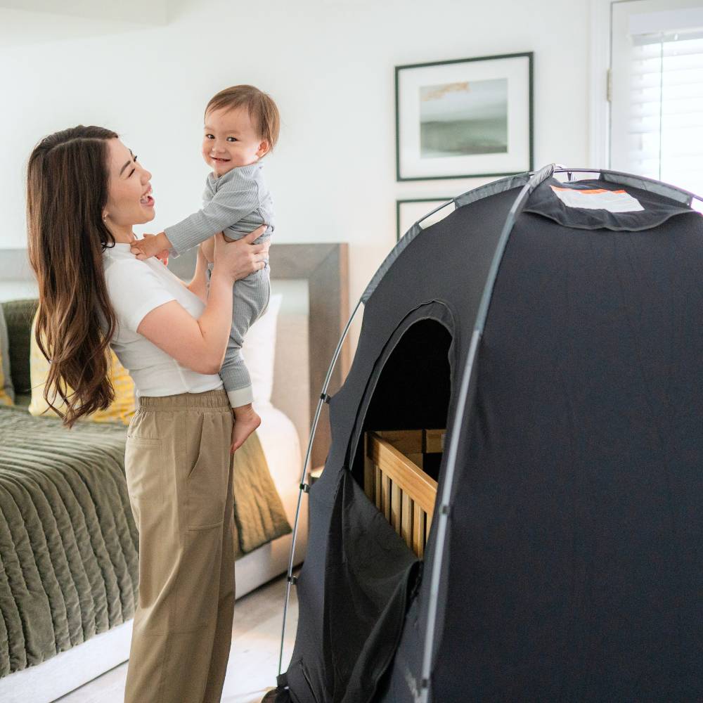 Woman holding a child next to a black tent in a bedroom
