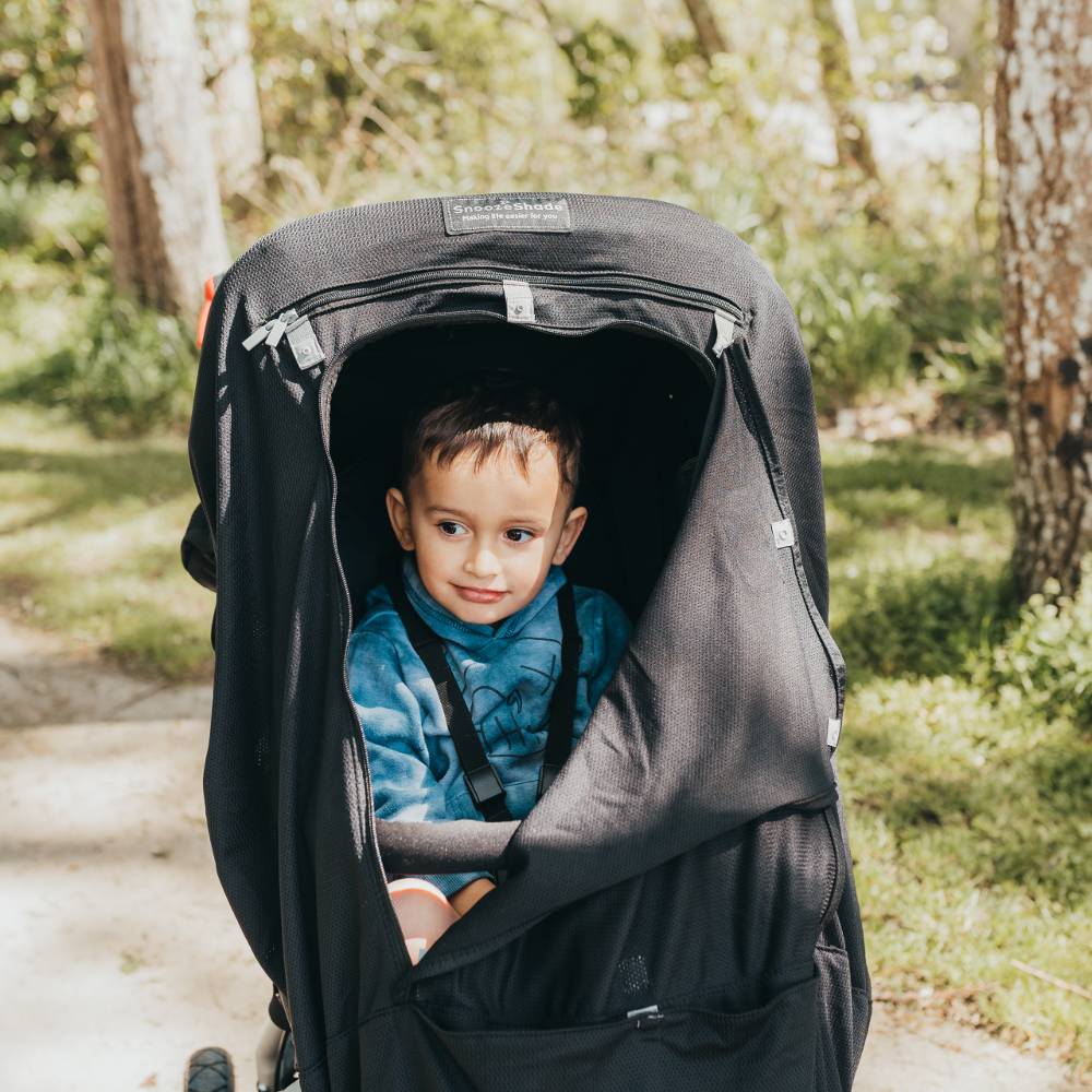 Child in a stroller with Snoozeshade blackout cover outdoors on a path with greenery