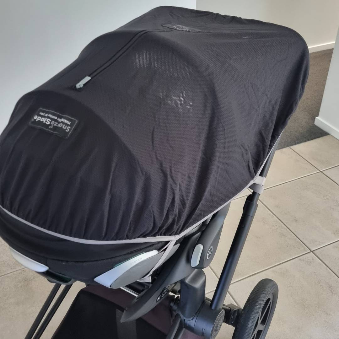 Black stroller cover on a stroller with a visible brand logo indoors.