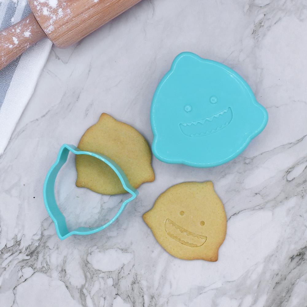 Cookie cutter with shark design and two shaped cookies on a marble surface