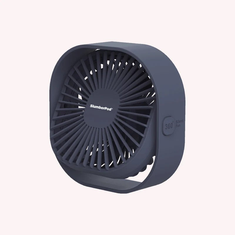 A compact, portable mini fan by SlumberPod in a dark slate gray color, shown from a three-quarters angle against a solid pale pink background.