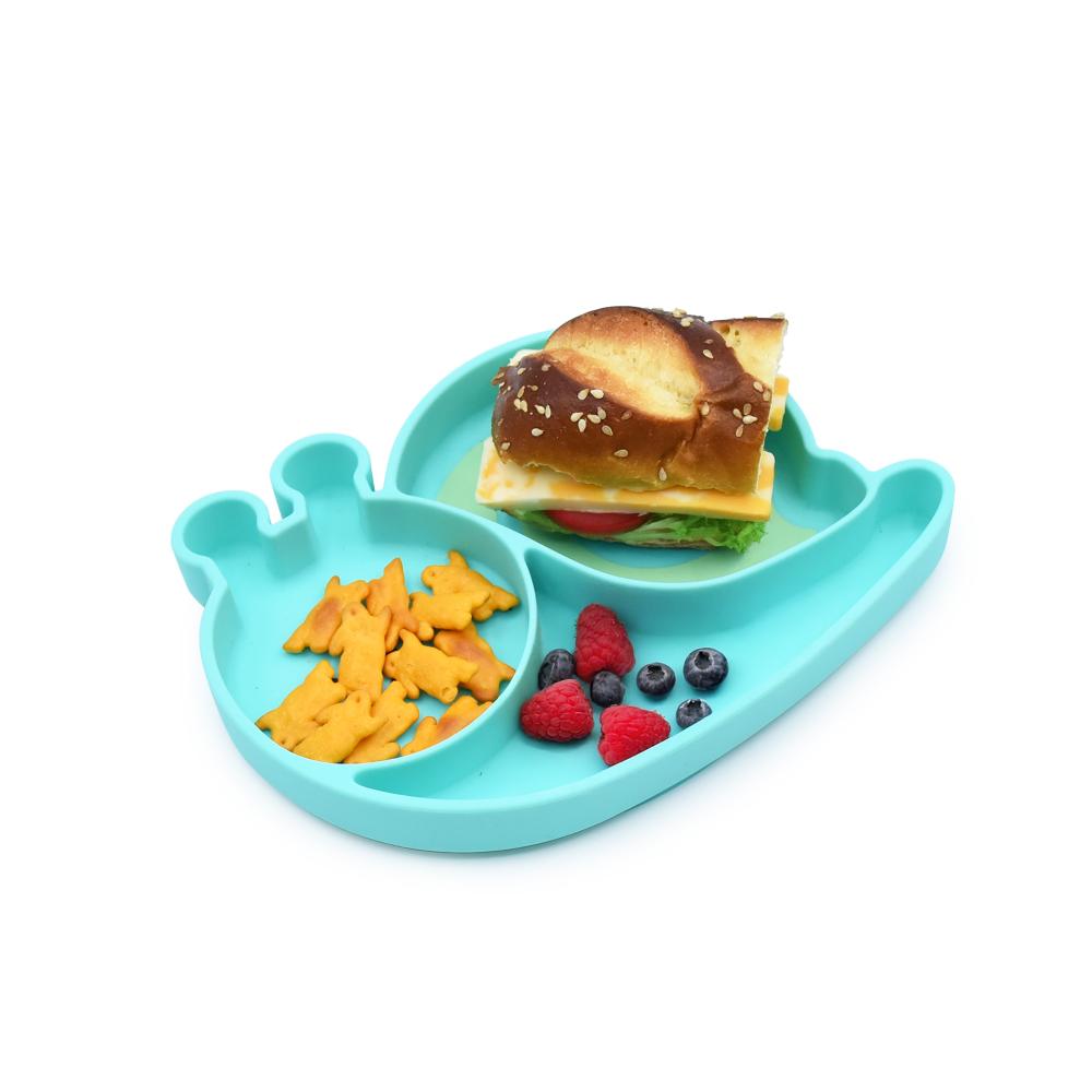 Turquoise snail-shaped silicone divided plate with sandwich, crackers, and berries on a white background