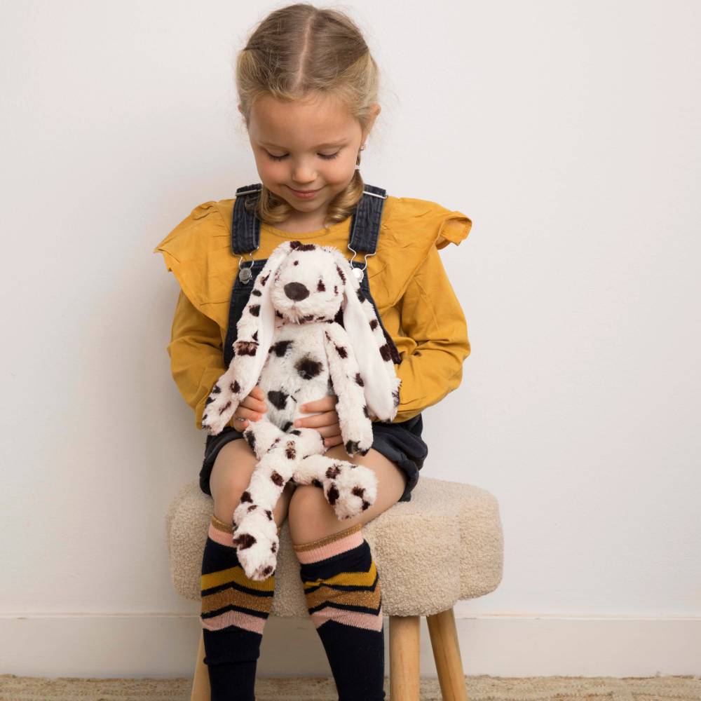 A young girl sitting on a stool holding a Happy Horse Rabbit Richie Special soft toy. 