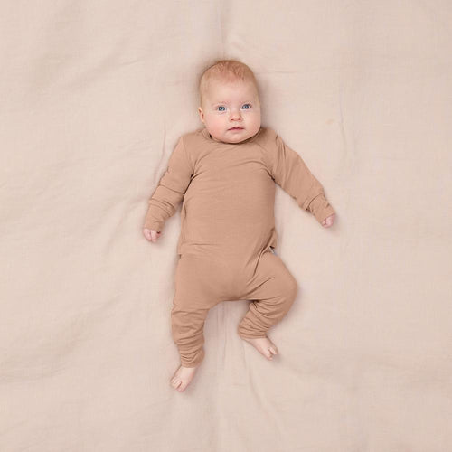 Baby wearing a brown onesie lying on a beige blanket