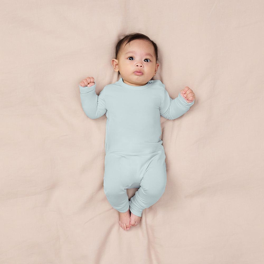 Baby wearing a light blue onesie lying on a beige blanket