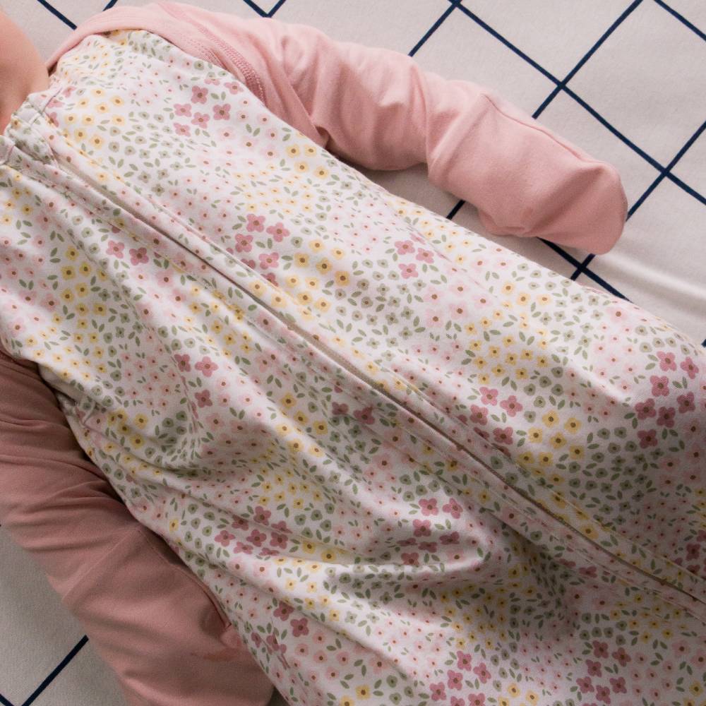 Person wearing a pink longsleeve mitten cardigan and floral sleeping bag on a checkered sheet