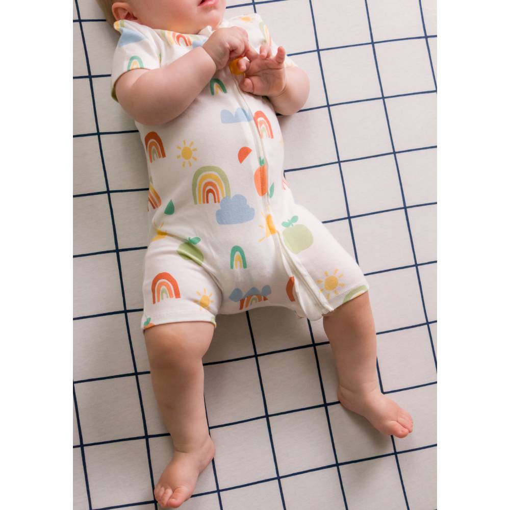 Baby lying on a checkered floor wearing a colorful onesie with rainbow and cloud patterns.