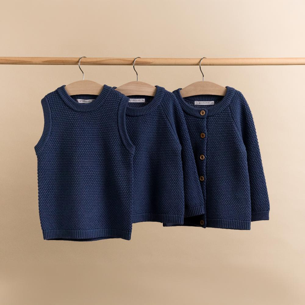 Three blue children's woolen knitted sweaters on hangers against a beige background