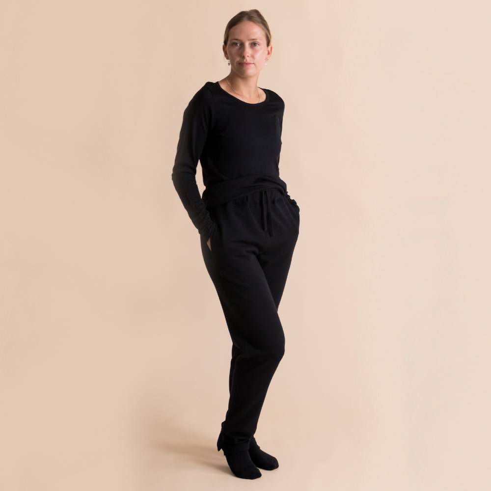 A woman modeling a black long-sleeve top and matching black drawstring sweatpants against a solid beige studio background.