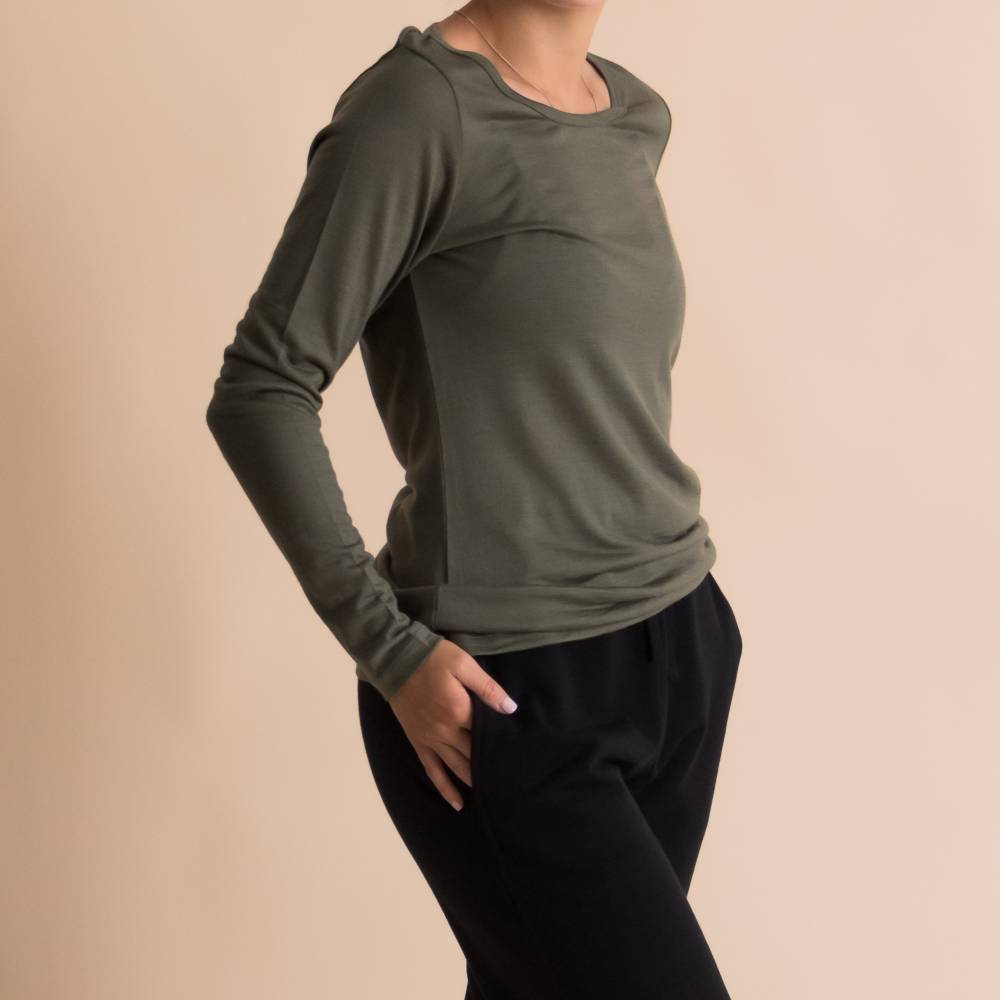 A woman wearing a fitted long-sleeve crewneck top in olive green, paired with black pants, shown against a solid beige studio background.