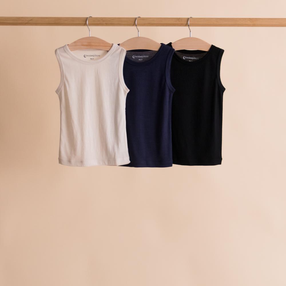 Three tank tops in white, navy, and black hanging on a rack against a beige background.