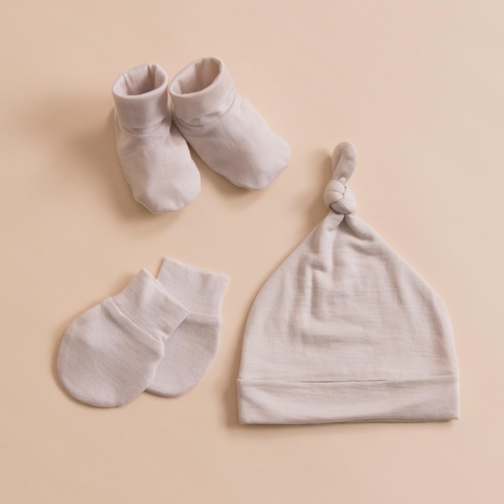 Merino & Tencel Baby hat, socks, and booties set on a beige background