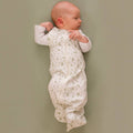 Baby in a white sleeping bag with green patterns lying on a plain background