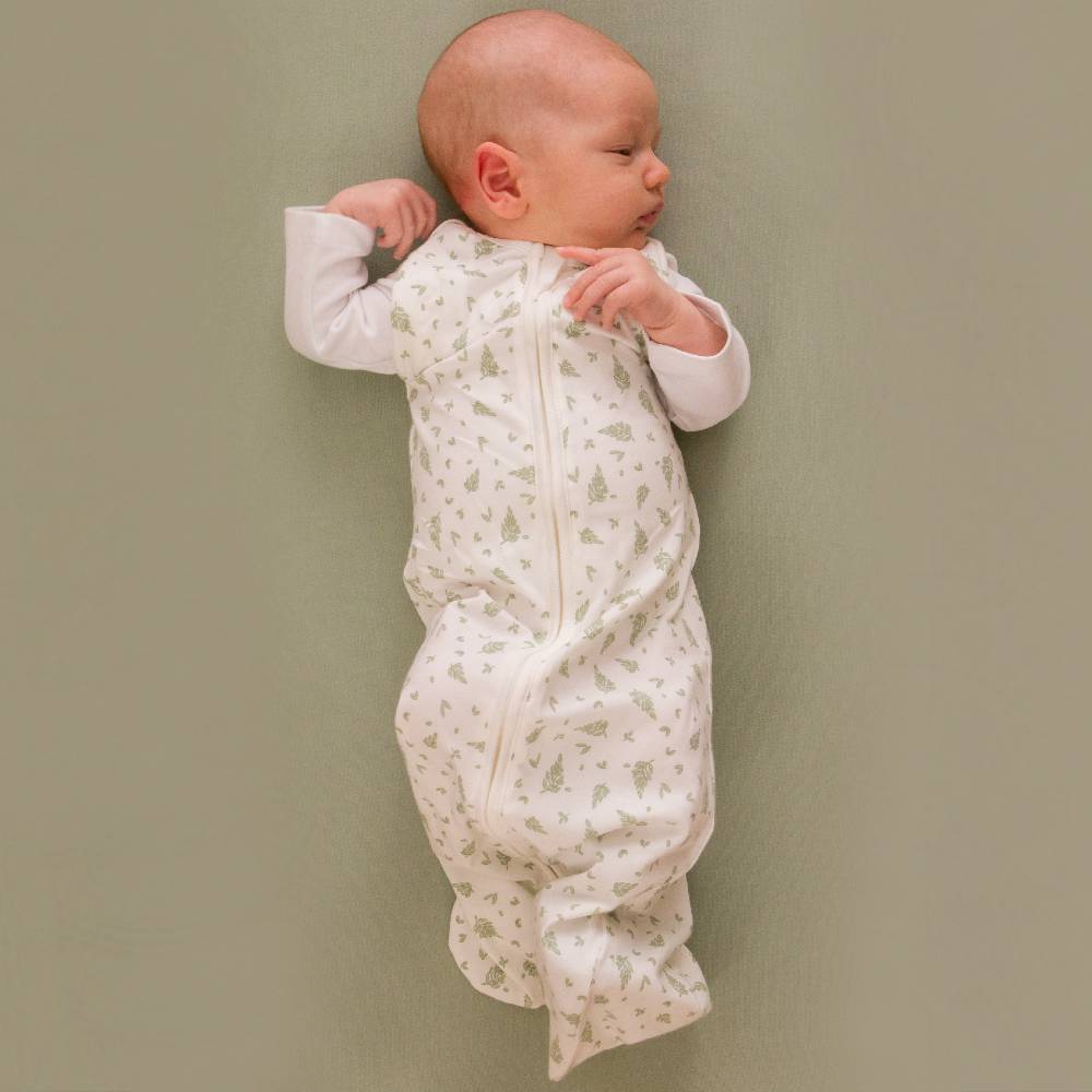 Baby in a white sleeping bag with green patterns lying on a plain background